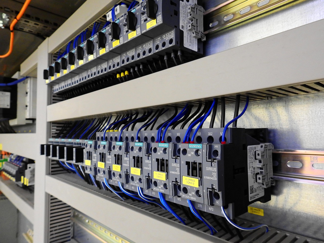 A grey electrical riser cupboard filled with circuit breakers and neatly run blue cabling