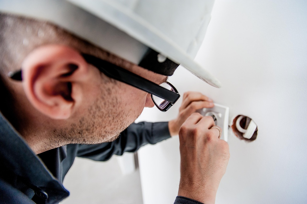 A licensed electrician in a hard hat wiring a wall socket